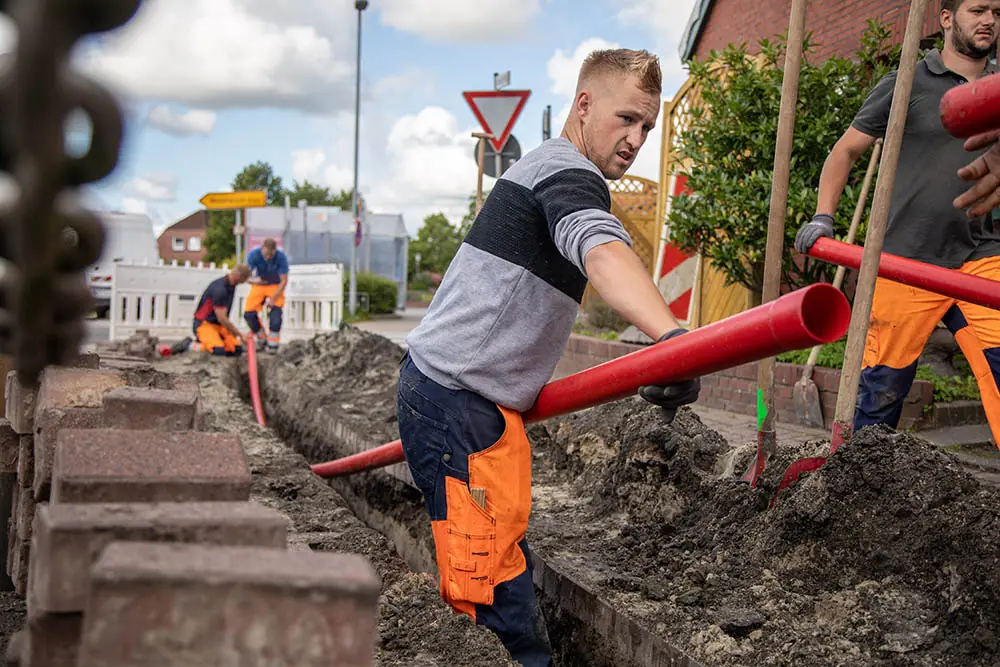 Monteur verlegt Schutzrohre im offenen Graben