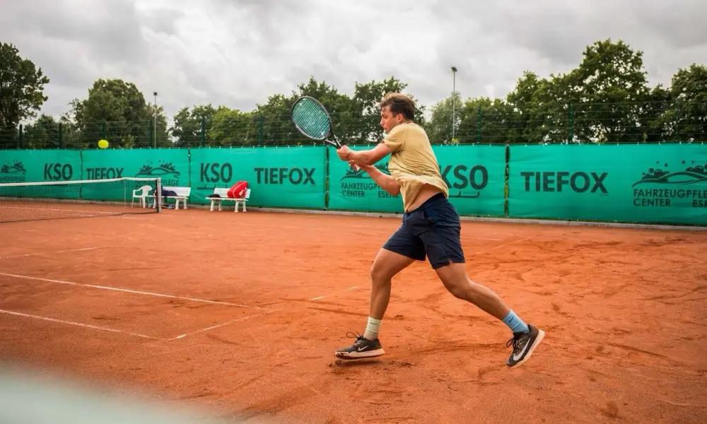 Tennisspieler auf dem Sandplatz vor KSO- und TIEFOX-Bandenwerbung